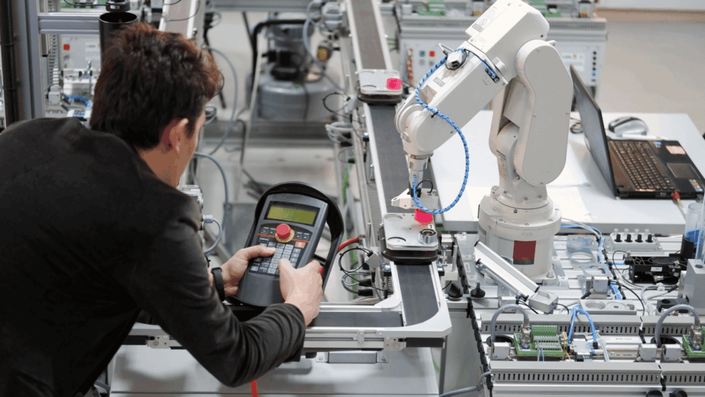 A technician operates a control panel for a robotic arm on an assembly line in a high-tech German manufacturing facility, representing industrial innovation that can impact company stocks.