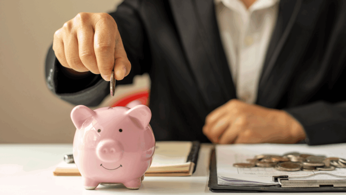 A person in a business suit places a coin into a pink piggy bank, illustrating the concept of saving and Long-term investing for financial security.