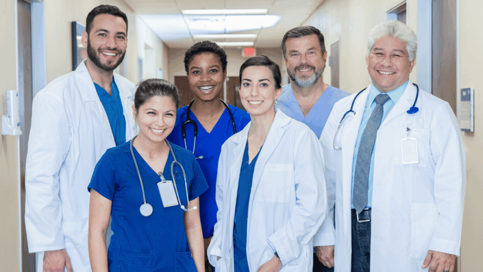 A diverse team of healthcare professionals standing together in a hospital hallway, representing the collaborative care provided through Health Insurance.